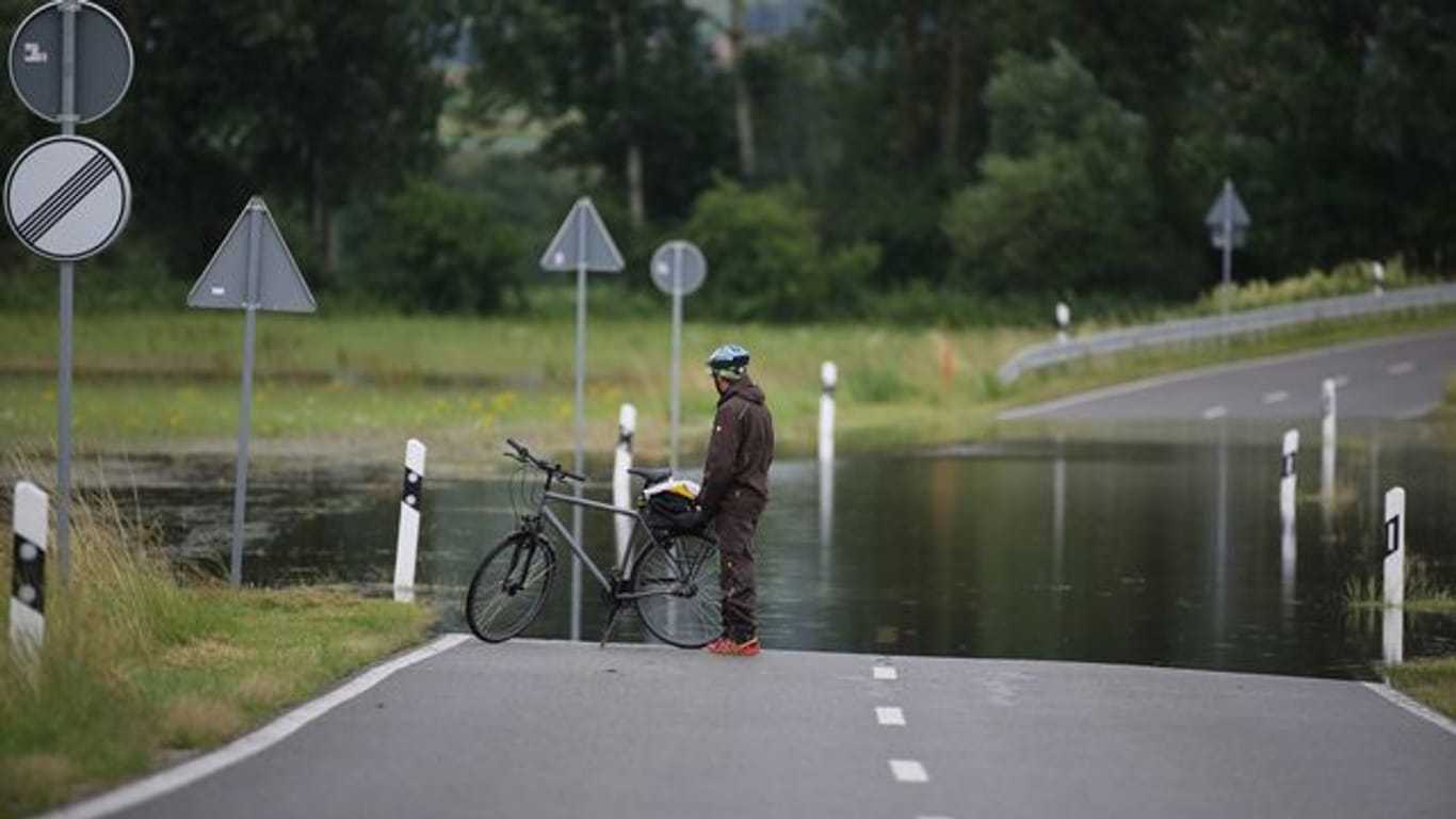 Ein Radfahrer steht an einer überfluteten Straße