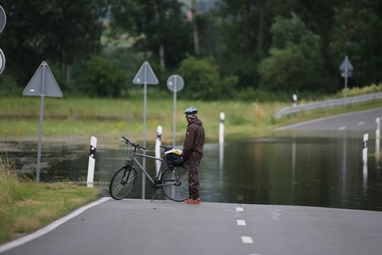 Ein Radfahrer steht an einer überfluteten Straße