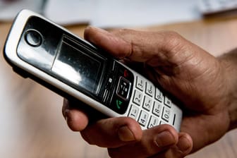 Die Hand eines älteren Menschen hält ein Telefon: Die Polizei Karlsruhe erhält in den letzten Tagen vermehrt Meldungen zu betrügerischen Telefonanrufen.