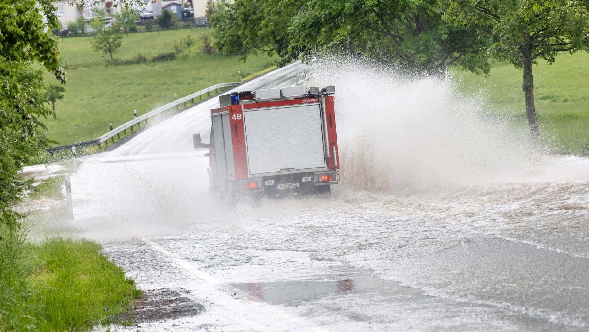 Feuerwehrauto fährt über eine überflutete Straße (Archivbild): Es drohen weiter Starkregen und Gewitter.