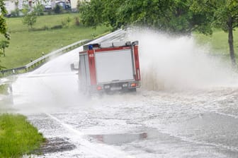 Feuerwehrauto fährt über eine überflutete Straße (Archivbild): Es drohen weiter Starkregen und Gewitter.