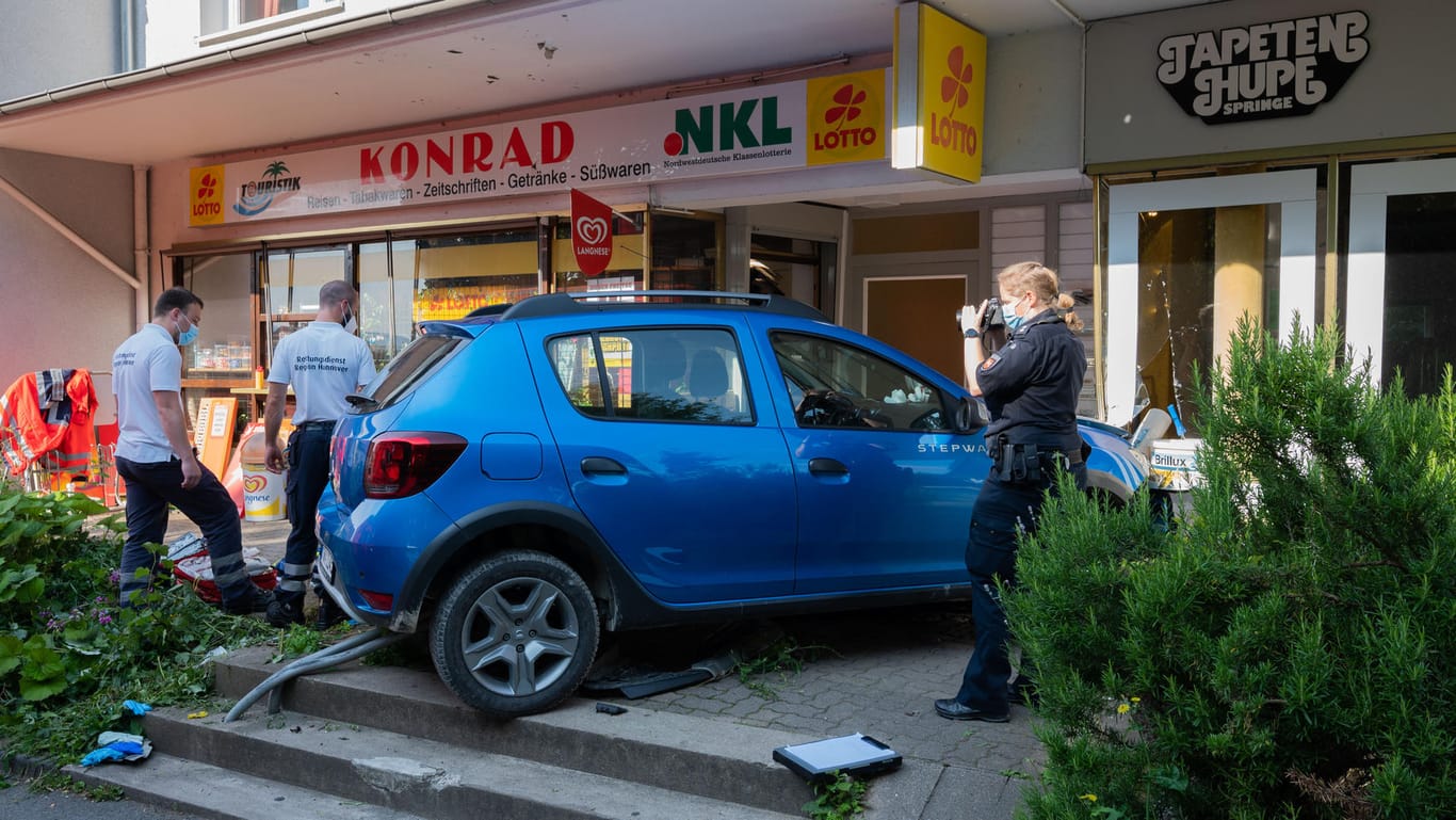 Einsatzkräfte von Rettungsdienst und Polizei stehen nach einem Unfall an einem Kleinwagen. Ein 76-jähriger Mann ist am Morgen in der Region Hannover mit seinem Fahrzeug in eine Schaufensterscheibe gekracht und gestorben.