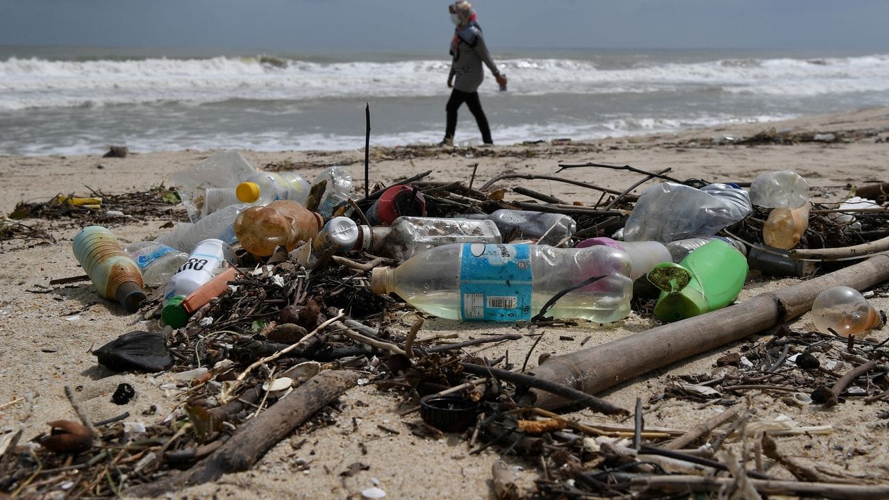 Eine Frau geht an einem Strand in Malaysia an Plastikmüll vorbei.