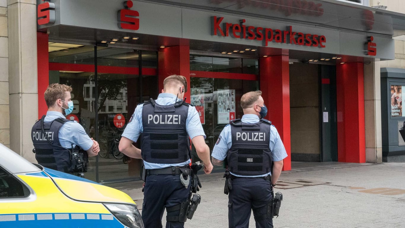 Polizisten stehen vor der überfallenen Hauptstelle der Kreissparkasse am Neumarkt: Nach der Tat sicherten Beamte Spuren, auch an der gegenüberliegenden Apostelnkirche.