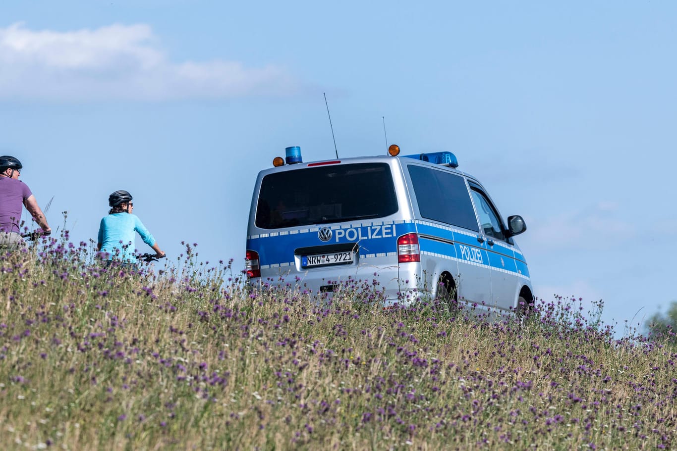Polizeiwagen neben Fahrradfahrern in der Rheinaue (Symbolbild): Nach einer Unfallflucht durch einen Radfahrer nahe Bonn sucht die Polizei den Unbekannten.