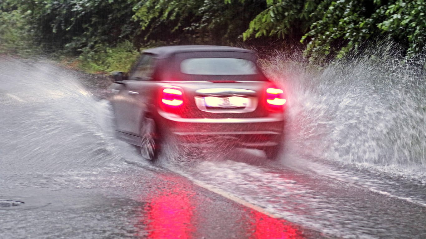 Ein Auto fährt über eine durch Regen überflutete Straße (Archivbild): Für Wuppertal wird in den kommenden Tagen Dauerregen erwartet.