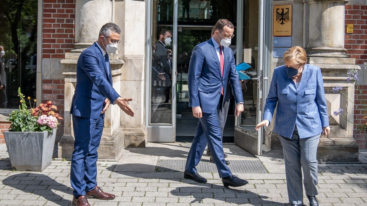 Angela Merkel sucht neben Jens Spahn und Lothar Wieler die Bodenmarkierung für das Gruppenbild.