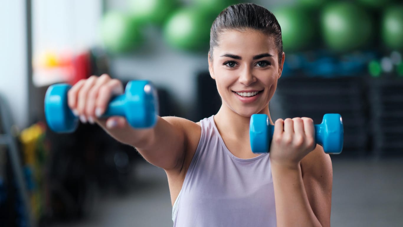 Eine Frau mit Kurzhanteln im Fitnessstudio. Wer trainiert ist, baut nach einer Sportpause schneller wieder Muskeln auf als Ungeübte.
