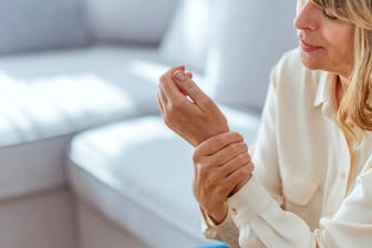 Frau mit Schmerzen im Handgelenk. Rheumatische Erkrankungen können in jedem Alter auftreten. Frauen sind dabei öfter betroffen als Männer.