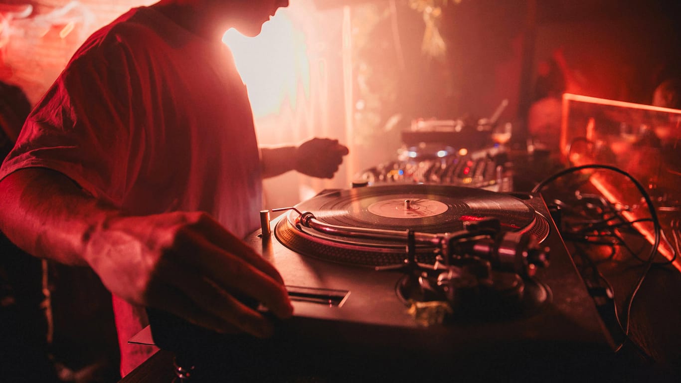 Ein DJ legt in einem Club auf (Symbolbild): In Stuttgart soll ein Modellprojekt mit Distanztrackern im Nachtleben starten.