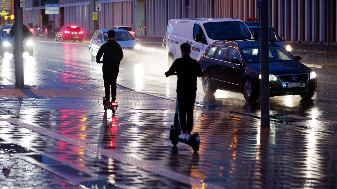 Zwei E-Scooter fahren bei Regenwetter durch die Kölner Innenstadt (Archivbild): Die Anbieter sträuben sich gegen ein Nachtfahrverbot.