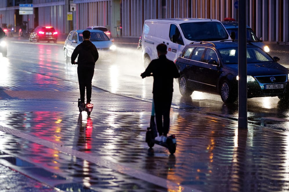 Zwei E-Scooter fahren bei Regenwetter durch die Kölner Innenstadt (Archivbild): Die Anbieter sträuben sich gegen ein Nachtfahrverbot.