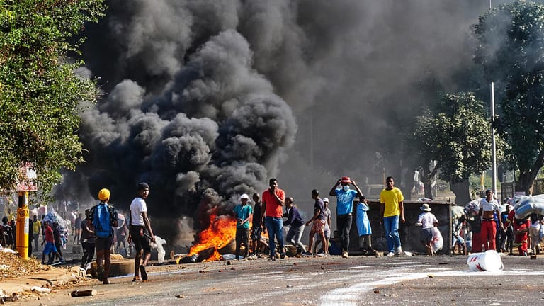 Durban: Plünderer stehen vor einem Einkaufszentrum neben einer brennenden Barrikade.