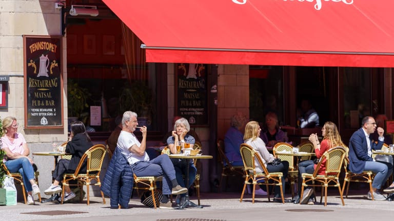 Menschen sitzen in Stockholm vor einem Cafe: In Schweden werden weitere Corona-Maßnahmen beendet.