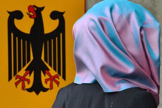 Eine junge Frau mit Kopftuch geht an einem Behördenschild mit dem Bundesadler vorbei.