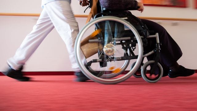Ein Pfleger eines Pflegeheims schiebt eine Bewohnerin mit einem Rollstuhl. Ein Pfleger eines Pflegeheims schiebt eine Bewohnerin mit einem Rollstuhl.