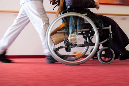 Ein Pfleger eines Pflegeheims schiebt eine Bewohnerin mit einem Rollstuhl.