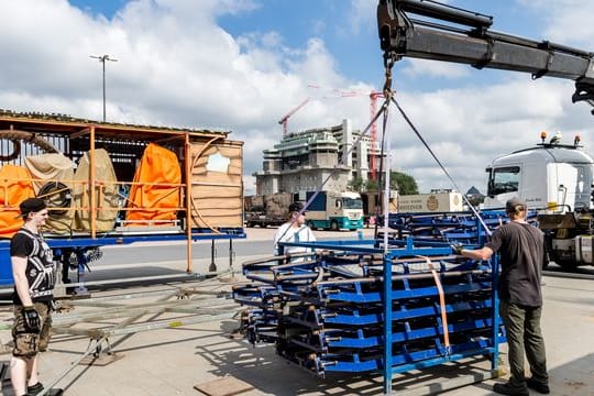 Mitarbeiter entladen mit einem Kran Gerüstteile des Fahrgeschäfts: Am 30. Juli wird das Volksfest eröffnet.
