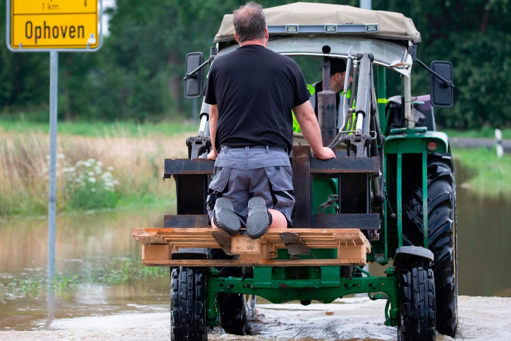 Zwei Männer auf einem Traktor auf einer überfluteten Straße in Ophoven: Vielerorts gibt es keine funktionierenden Sirenenanlagen mehr.
