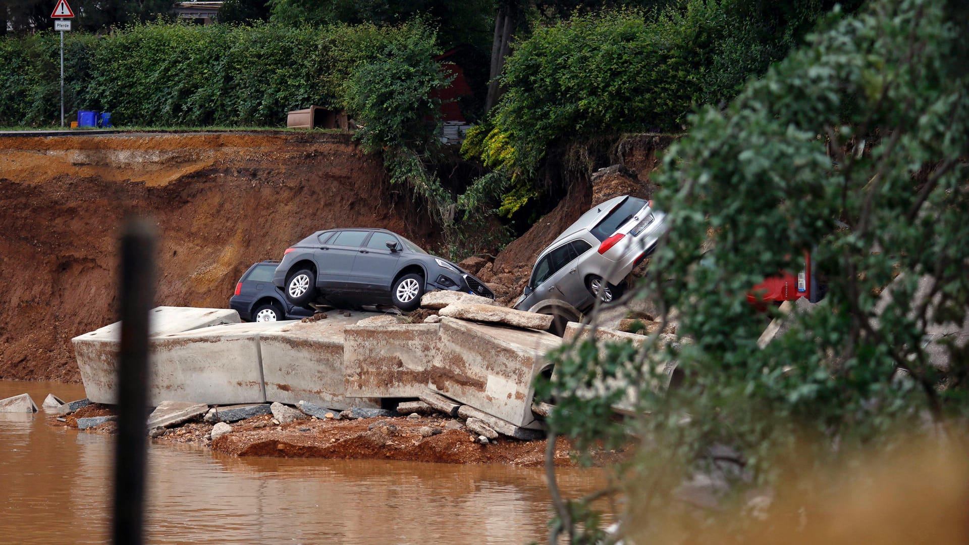 Autos liegen in einer vom Wasser ausgeschwemmten Grube: Das Hochwasser hat viele Straßen zerstört.