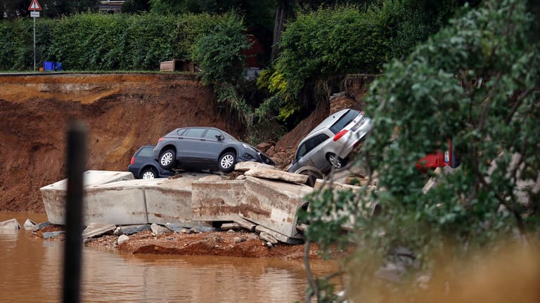 Autos liegen in einer vom Wasser ausgeschwemmten Grube: Das Hochwasser hat viele Straßen zerstört.