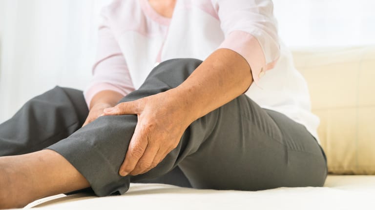 Eine Frau fasst sich ans Bein: Anzeichen für eine Thrombose können Schmerzen und Schwellungen am Bein sein.