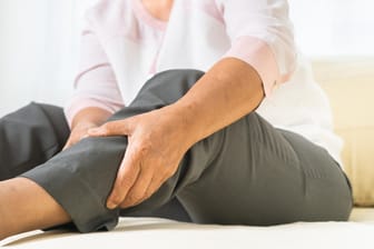 Eine Frau fasst sich ans Bein: Anzeichen für eine Thrombose können Schmerzen und Schwellungen am Bein sein.