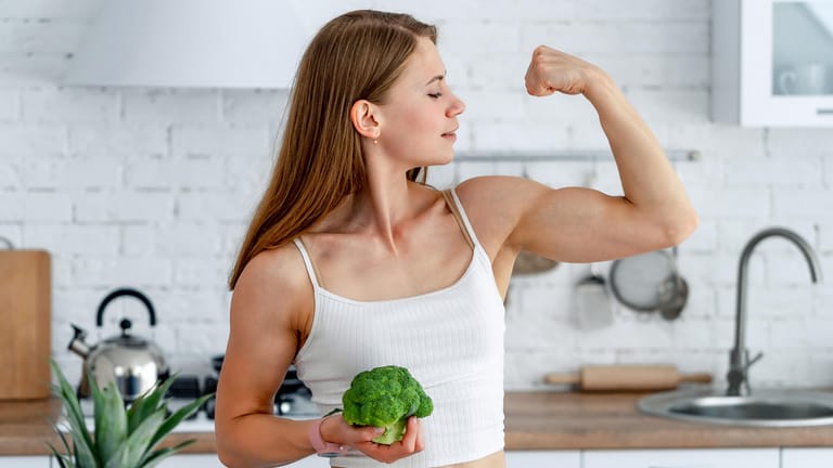 Frau mit Brokkoli: Für einen gesunden Muskelaufbau sind neben ausreichend Eiweiß auch zahlreiche Nährstoffe von großer Bedeutung.