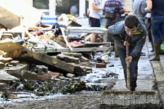 Ein Junge fegt eine verwüstete Straße in Belgien: Schwere Unwetter haben Teile des Ostens und Südens des Landes verwüstet.