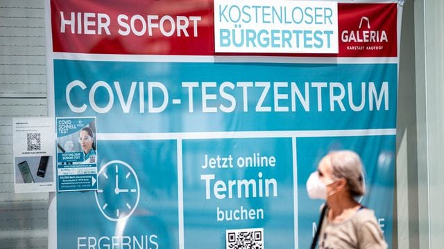 Eine Frau mit Maske läuft an einem Corona-Testzentrum am Berliner Alexanderplatz vorbei.