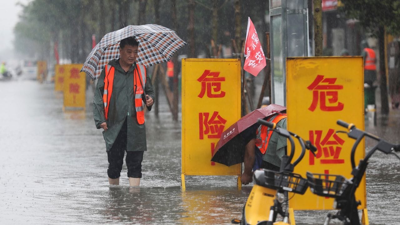 Mitarbeiter stellen Warnschilder auf mit der Aufschrift "Gefahr!" in einem überschwemmten Gebiet im Kreis Wuzhi in der zentralchinesischen Provinz Henan.