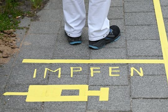 Ein Mann steht hinter einer Bodenmarkierung "Impfen"