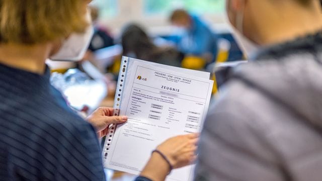 Die Klassenlehrerin übergibt das Zeugnis eines Schülers