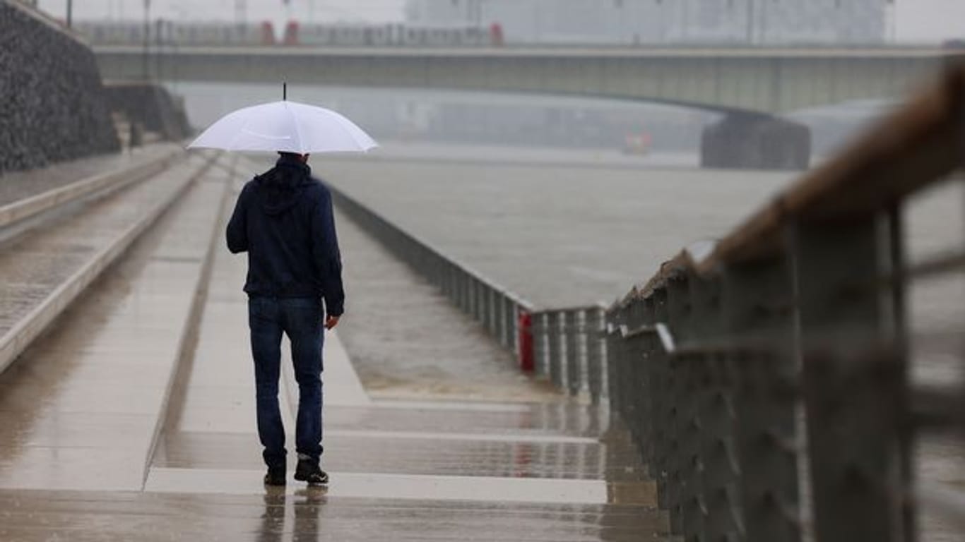 Ein Mann steht mit Regenschirm an der Freitreppe am Rheinufer