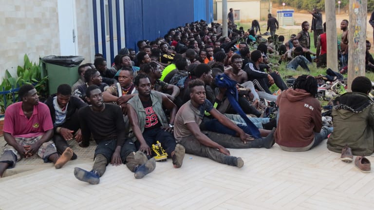 In der spanischen Nordafrika-Exklave Melilla: Eine Gruppe von Menschen sitzt vor einem Aufnahmezentrum für Migranten.