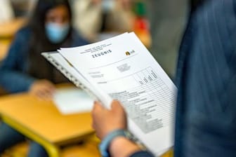 Die Klassenlehrerin hält das Zeugnis eines Schülers in der Hand