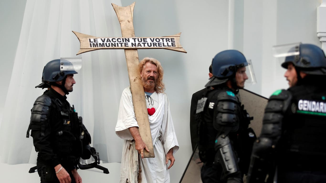 Ein Mann hält ein Kreuz mit der Aufschrift "Vakzine töten deine natürliche Immunität" am Rande von teilweise gewalttätigen Protesten in Paris.