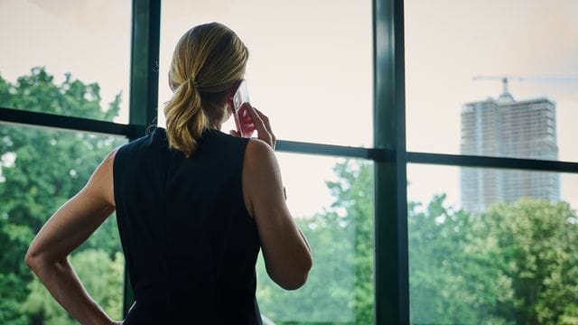 Eine Frau steht in einem Büro am Fenster und telefoniert