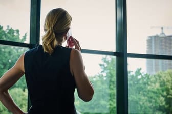 Eine Frau steht in einem Büro am Fenster und telefoniert