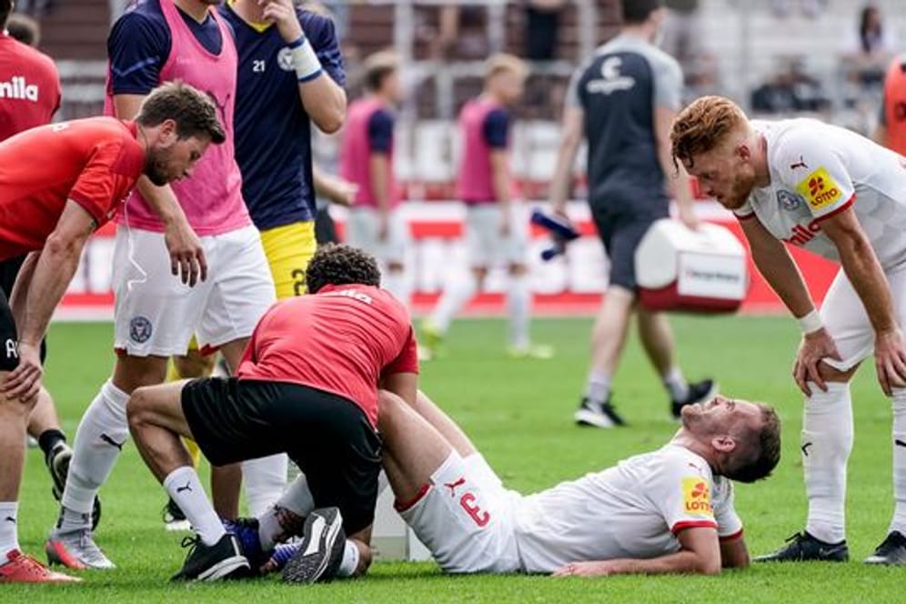 Kiels Marco Komenda wird auf dem Platz behandelt während Kiels Mikkel Kirkeskov (r) zuschaut. Der Abwehrspieler hat sich den Mittelfuß gebrochen.