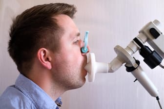 Mann beim Lungenfunktionstest: Bei der Spirometrie atmet man nach Anweisung in ein Mundstück, wobei Menge und Geschwindigkeit der ein- und ausgeatmeten Luft erfasst werden.