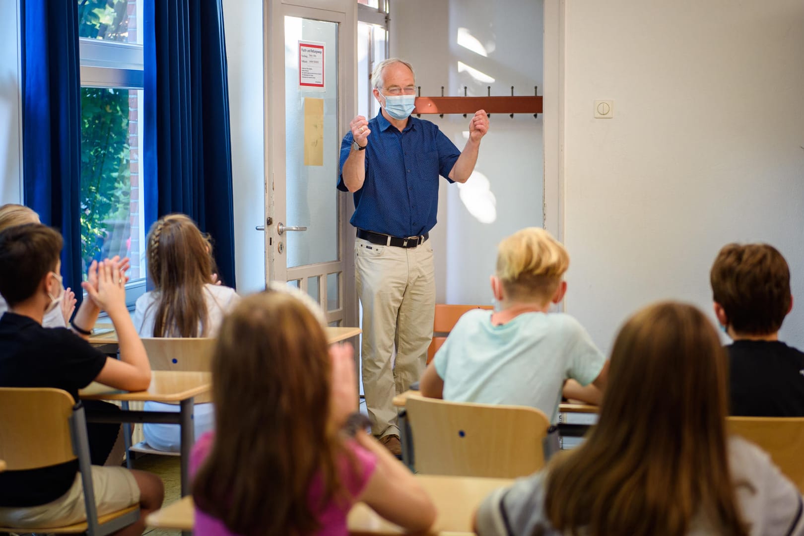 Ein Kieler Schulleiter begrüßt Schülerinnen und Schüler am ersten Tag des Schuljahres: Auch zwölf Monate später prägen Schutzmaßnahmen gegen das Coronavirus die Unterrichtsbedingungen.