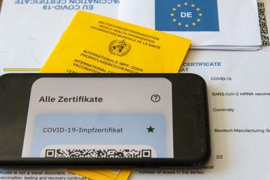Ein Impfpass und ein Smartphone, auf dem die App CovPass läuft, liegen auf einem Impfzertifikat.