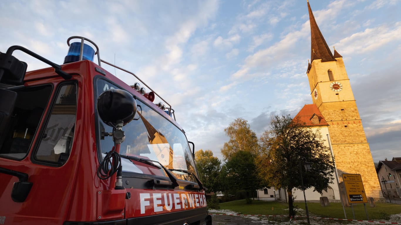 Ein Fahrzeug der Feuerwehr steht vor dem Kirchturm von Halfing: Der Turm wurde durch ein Unwetter schwer beschädigt.