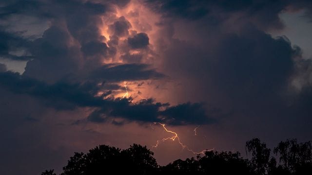 Ein Blitz hellt hinter dunklen Wolken auf