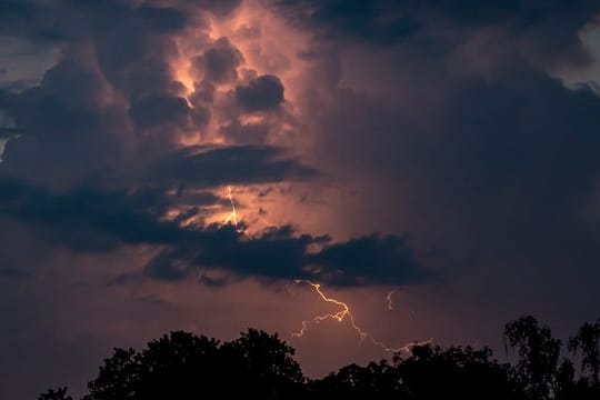 Ein Blitz hellt hinter dunklen Wolken auf