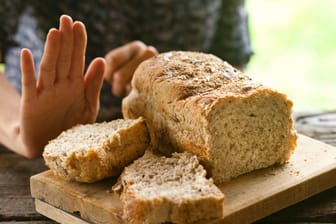 Ein angeschnittenes Brot und eine Hand mit ablehnender Geste.