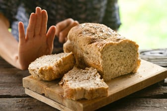 Ein angeschnittenes Brot und eine Hand mit ablehnender Geste.