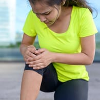 Eine junge Frau greift sich an den Unterschenkel. Wer starken Muskelkater hat, sollte sich beim Training nicht überstrapazieren.