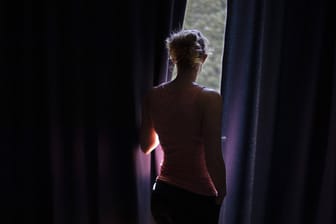 Eine Frau schaut aus einem Fenster (Symbolbild): Gewalt in Beziehungen sei ein Problem in der Mitte der Gesellschaft, wie ein Kölner Streetworker sagt.